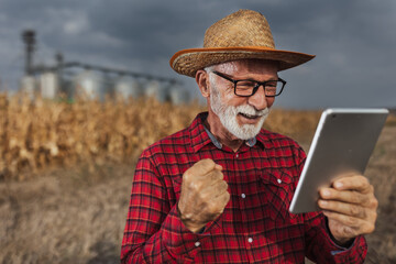 Satisfied farmer looking at tablet in front of silos in field