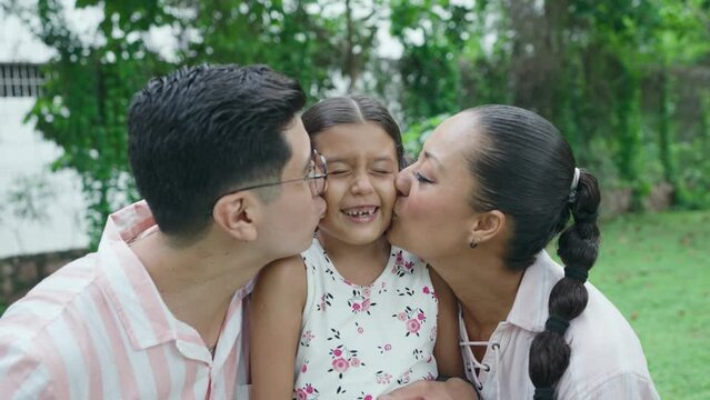 Mom and Dad Give Smiling Daughter a Kiss on the Cheek