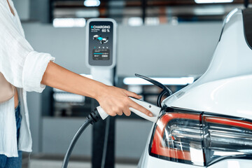 Young woman travel with EV electric car to shopping center parking lot charging in downtown city...