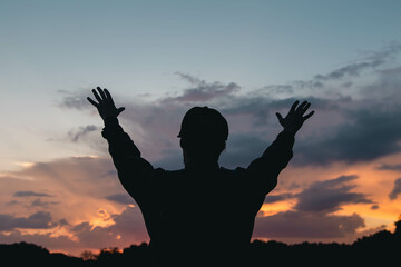 A young Christian man with a beard in nature raises his hands to the sky, thanks God, praises.