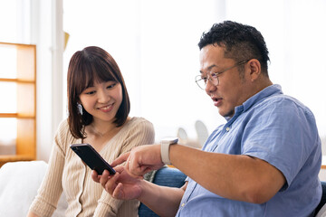 Fototapeta premium リビングでスマートフォンを使う男女