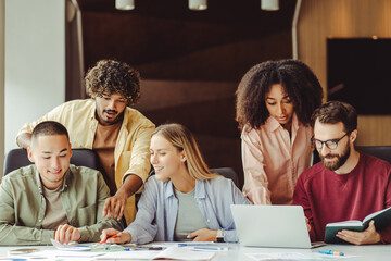 Group of smiling multiracial university students using laptop studying  together, education concept. Young startup team, colleagues meeting, working, planning strategy in office. Successful business