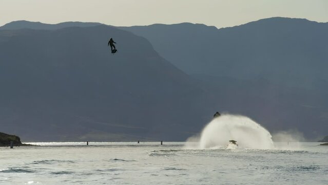 Man flying over lake with jetpack with other people having fun.