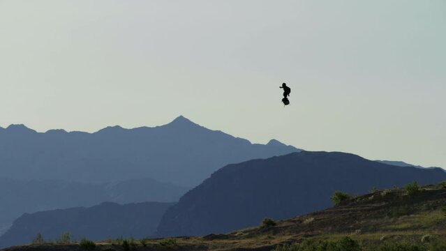 Man flying high above the ground with jet pack with mountains in distance