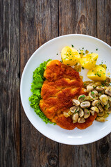 Crispy breaded seared chicken cutlet with fried white mushrooms and boiled potatoes on wooden table
