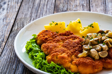 Crispy breaded seared chicken cutlet with fried white mushrooms and boiled potatoes on wooden table
