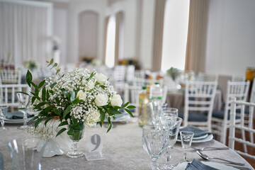 Serving the festive table with dishes, glasses, numbers and a bouquet of flowers. Restaurant interior.