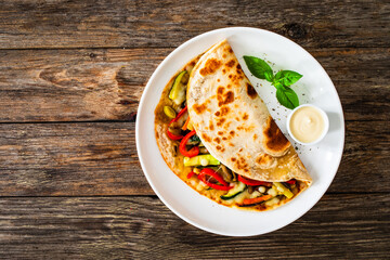 Italian piada wraps - piadina filled with fried vegetables and mozzarella cheese on wooden table
