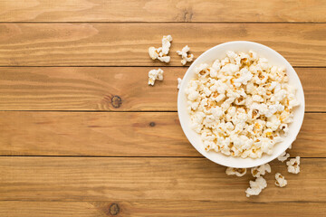 Tasty popcorn in bowl on wooden background, top view