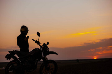 silhouette of a motorcyclist at sunset with an enduro motorcycle, the concept of the romance of...