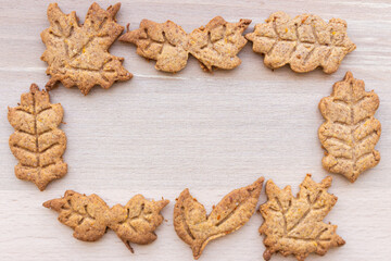Fototapeta premium Autumn leaf shaped cookie in frame. Gingerbread pastry with copy space. Autumn festive cookies. Handmade bakery. Gingerbread cookie form. Homemade dessert in sunlight. Autumn mood.
