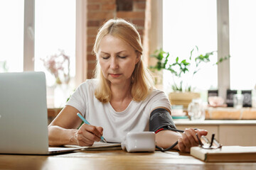 Senior woman measuring her blood pressure. Retired uses medicine digital device tonometer for...