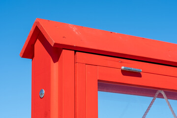 Bright orange wooden frame section with metal hinge and linen rope. Clear blue sky in the...