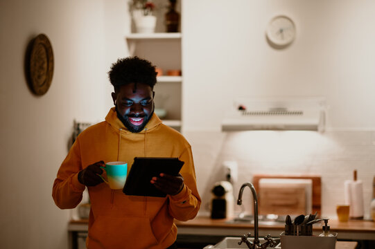 Interracial man is holding a mug of tea and having a conference call on a tablet