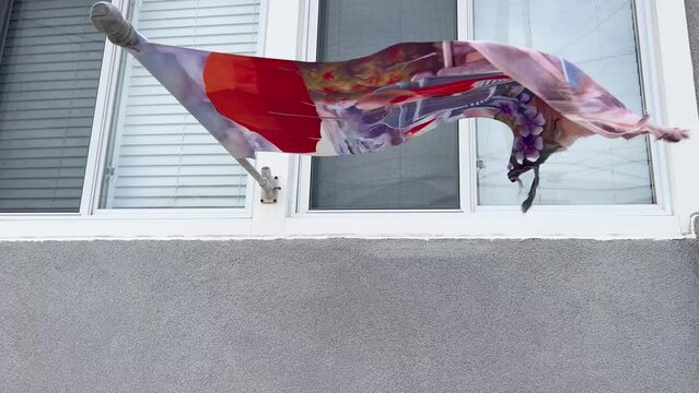 Torn decorative flag flag in front of a gray house seen flapping in a strong wind