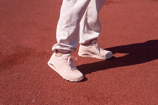 Woman legs in sports wear and pink sneakers standing on a tartan path in a park