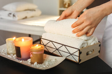 There are lit aromatic candles on the table, a spa center employee puts towels for treatments. - obrazy, fototapety, plakaty