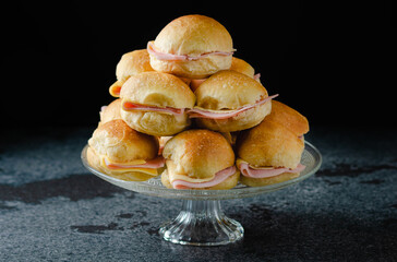 Butter figacitas, small ham and cheese sandwich. Close-up, glass plate, on marble, granite table, black background..