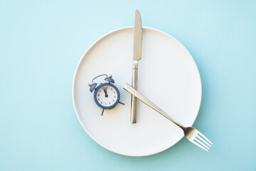 Intermittent fasting concept. Healthy eating, diet. White plate with cutlery and clock.