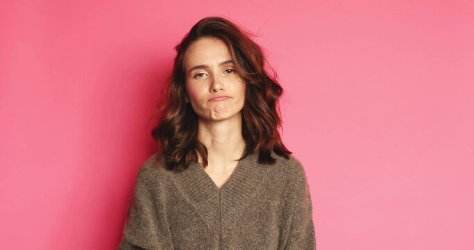 Boring cute brunette young woman in sweater posing isolated on pink background in studio. People lifestyle concept. Looks around, bites her lips, misses and waiting for something, gloomy and yawn