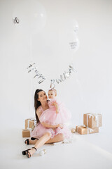 Smiling young caucasian lady sitting of floor with cute daughter in studio fulfilled with festive...