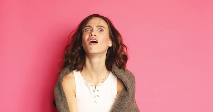Frustrated curly brunette woman portrait. Nervous breakdown. Pissed off lady yelling with anger isolated on pink background.