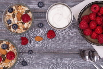 Homemade granola with nuts, raspberries and blueberries, yogurt on a wooden rustic table, top view,...