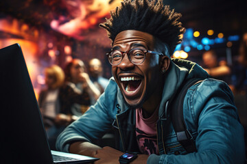happy black young man looks at laptop screen and laughs in a cafe - obrazy, fototapety, plakaty