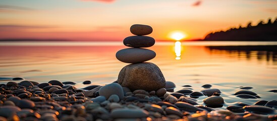 Zen stones on the beach at sunset creating a balanced pebble pyramid silhouette against the sea background evoking the concept of harmony and calmness