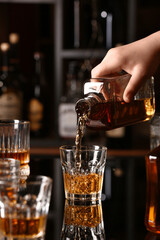 Woman pouring tasty rum from bottle into glass at table in bar