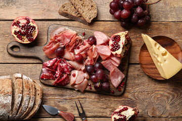 Board with assortment of tasty deli meats, cheese and bread on wooden background
