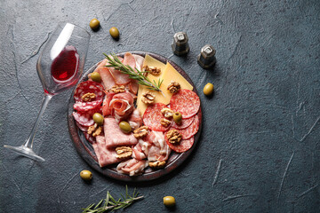 Plate with assortment of tasty deli meats, cheese and wine glass on black background