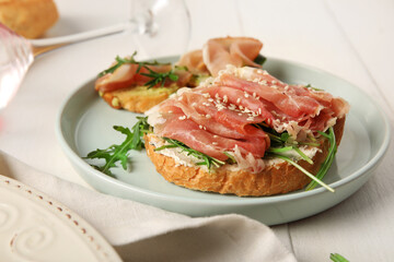 Plate of tasty bruschettas with ham on white wooden background