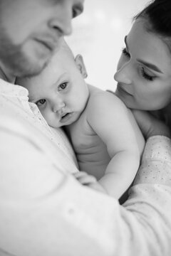 Close up of little naked baby girl being embraced by loving parents at studio. Monochrome photo of beautiful caucasian family of three enjoying every moments during parenting.