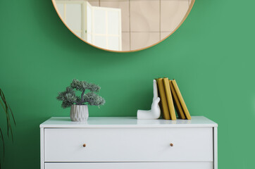 Stylish holder for books with bonsai on commode near green wall