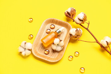 Composition with bottle of essential oil, glass stones and cotton flowers on yellow background