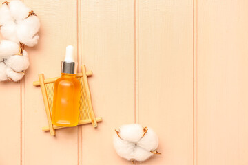 Bottle of essential oil and cotton flowers on color wooden background