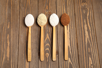 Wooden spoons with different types of flour and cacao on brown wooden background