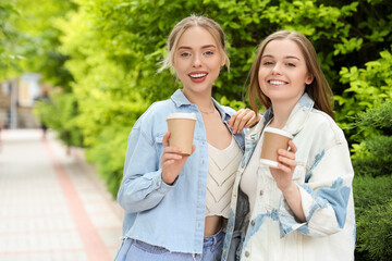 Young sisters with cups of coffee on city street