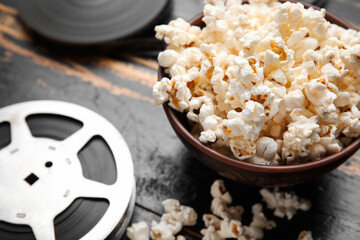 Bowl with tasty popcorn and film reels on black wooden background