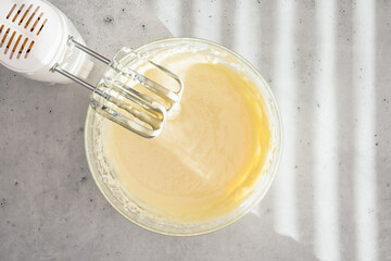 Cheesecake batter in a glass bowl. Cheesecake recipe, preparation process. Mixing batter in a glass bowl, flat lay - obrazy, fototapety, plakaty
