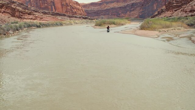Cinematic shot of man on hoverboard flying over desert river