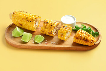 Wooden board with cut tasty grilled corn cob and sauce on yellow background