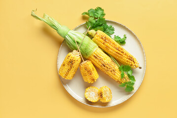 Plate with tasty grilled corn cobs and parsley on yellow background