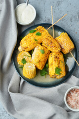 Plate with tasty grilled corn cob skewers and parsley on blue background