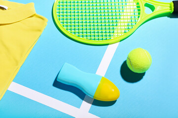 Bottle of sunscreen cream, t-shirt, tennis racket and ball on color background