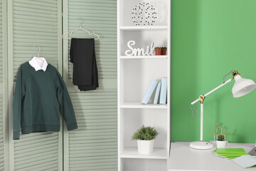Shelving unit with decor, lamp stylish school uniform hanging on folding screen in room