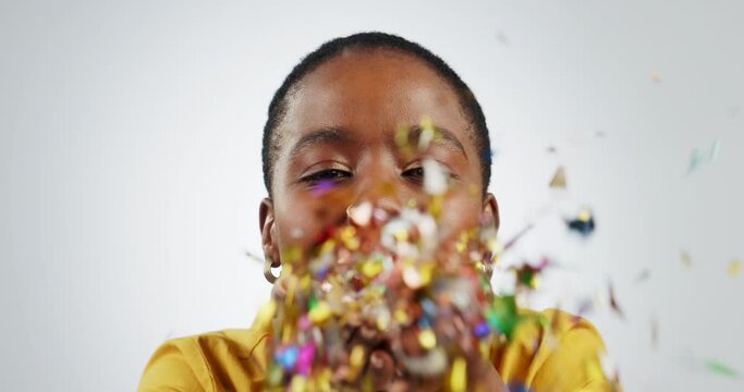 Blowing confetti, face and a black woman on a studio background for celebration or party. Happy, portrait and a young excited African girl or person with decoration for confidence, fun and pride