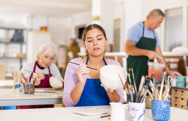 Woman is learning to paint on ceramic cup in a handicraft workshop, handmade art and hobby concept