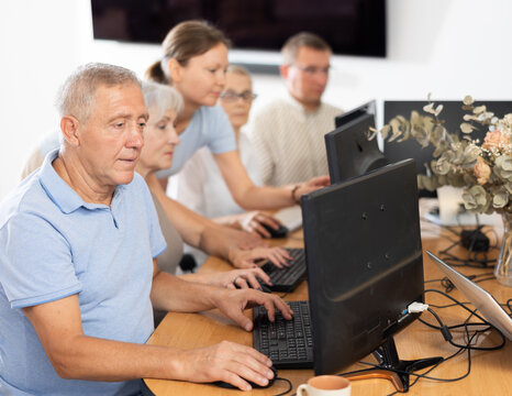 Older gentleman engrossed in exploring digital realm at internet cafe, using computer, demonstrating curiosity of modern seniors towards technology